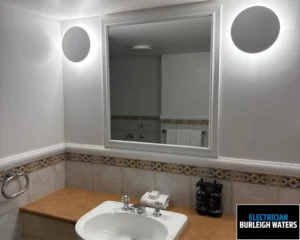 Modern bathroom with a white sink, wooden countertop, mirror, and round wall light.